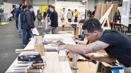 Un apprenti menuisier montre son savoir-faire en travaillant une pièce de bois lors d'un salon de l'apprentissage à Poitiers (Vienne), le 9 mars 2024. (JEAN-FRANCOIS FORT / HANS LUCAS / AFP)