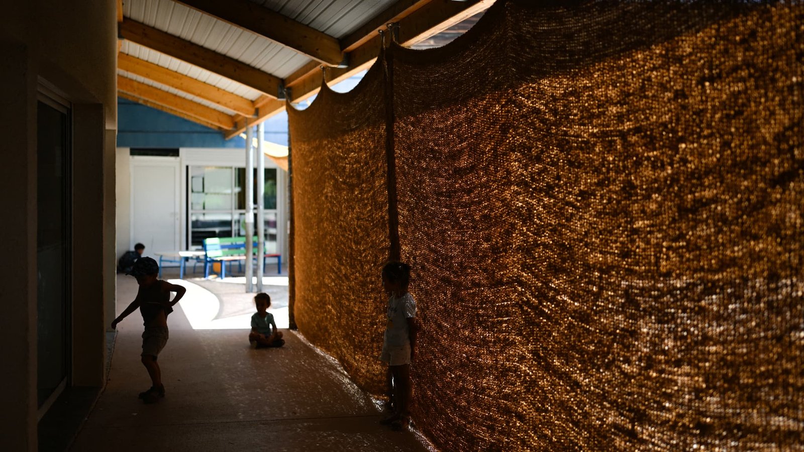 Des enfants se protègent du soleil à l'école Jean Ponsy de Grabels, près de Montpellier (sud de la France), où le programme « Racine » est expérimenté pour réduire la température de 7 degrés Celsius, le 23 juin 2026. Le programme « Racine » repose sur un ensemble de mesures incluant la protection solaire, des dispositifs de rafraîchissement et la ventilation