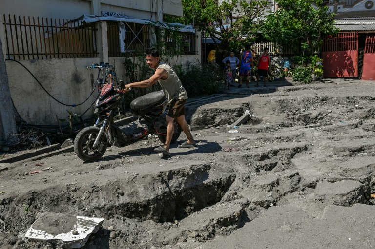 Un habitant pousse sa moto sur une route endommagée après un séisme de magnitude 7,8 à General Santos, le 9 juin 2026 aux Philippines (AFP/Archives - Jam STA ROSA)