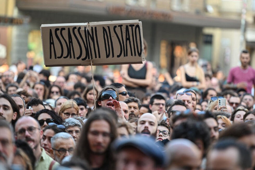 A protester holds a placard reading in Italian "State murderers" above a crowd during a protest following the death of Abderrahim Fakir