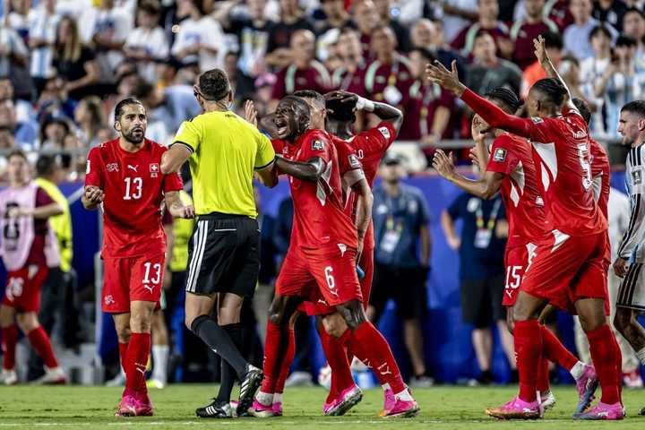 Les joueurs suisses entourent l'arbitre Joao Pinheiro qui s'apprête à donner un carton rouge Breel Embolo, lors du match de la Coupe du monde 2026 opposant l'Argentine à la Suisse, le 11 juillet 2026, à Kansas City. (STEFAN KOOPS / AFP)